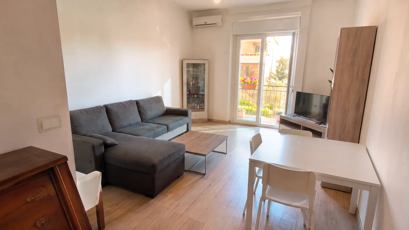 Zona giorno con divano ad angolo, tavolo e porta finestra sul balcone, sgombrata e riordinata (dopo)