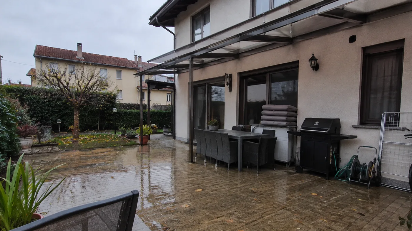 Veranda sul giardino con tavolo, sedie e barbecue, col sole e la pavimentazione asciutta (prima)